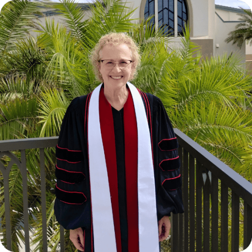 Smiling woman in academic robe standing beside palm trees