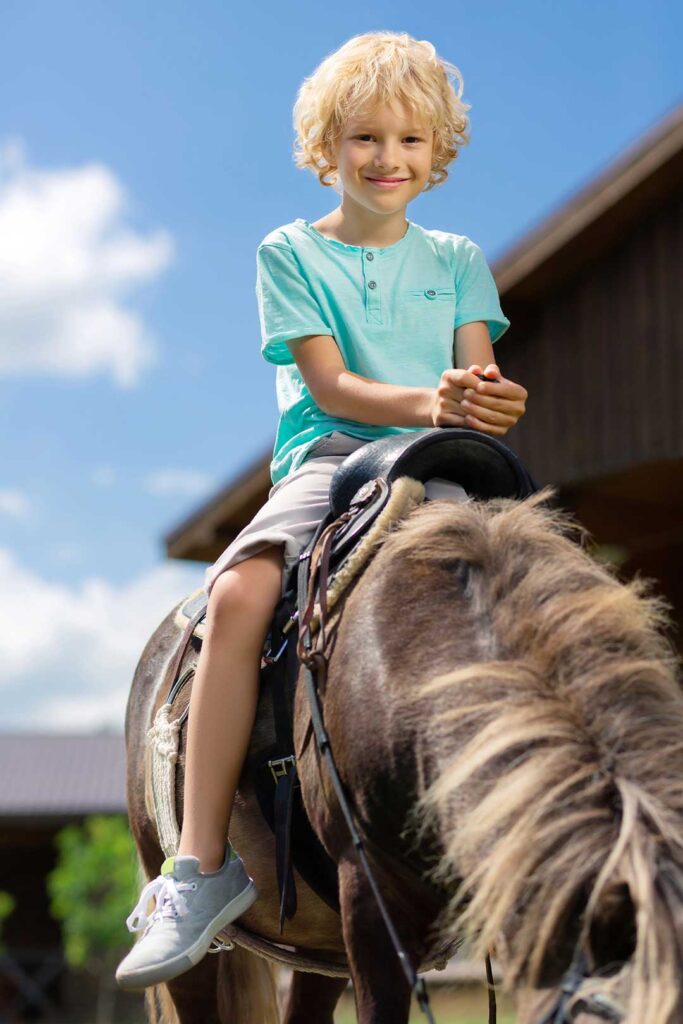 Smiling child riding a pony outdoors under blue sky