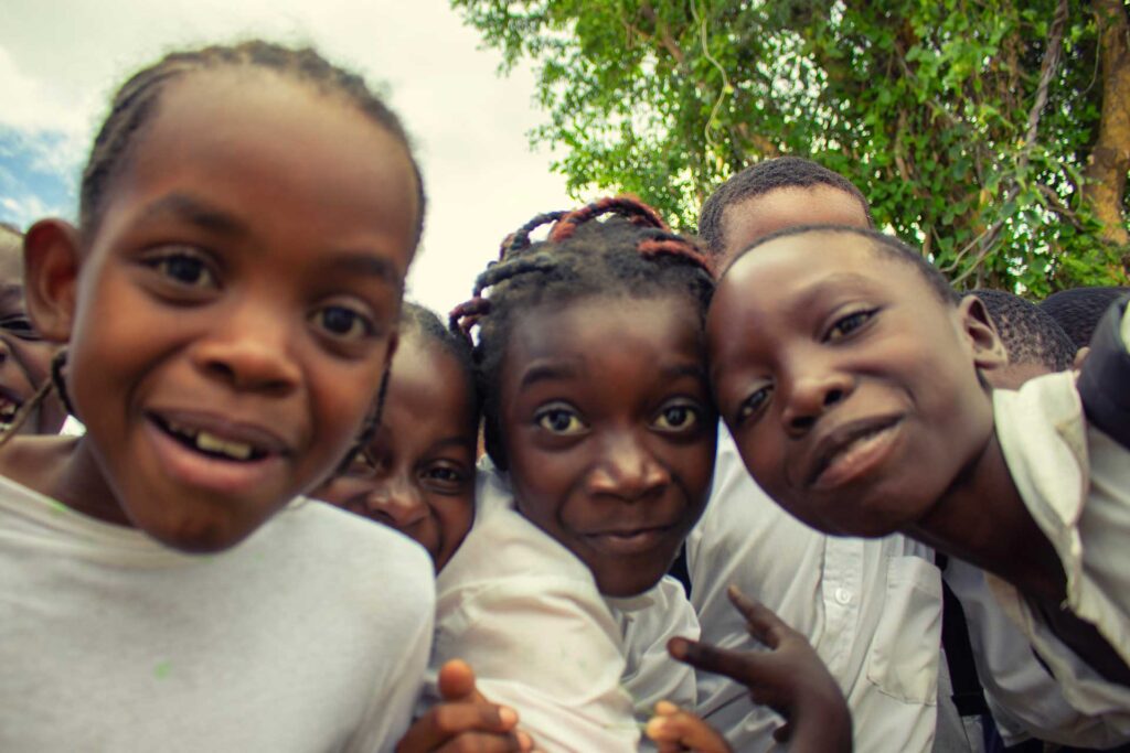 Four smiling children crowd around a camera outdoors